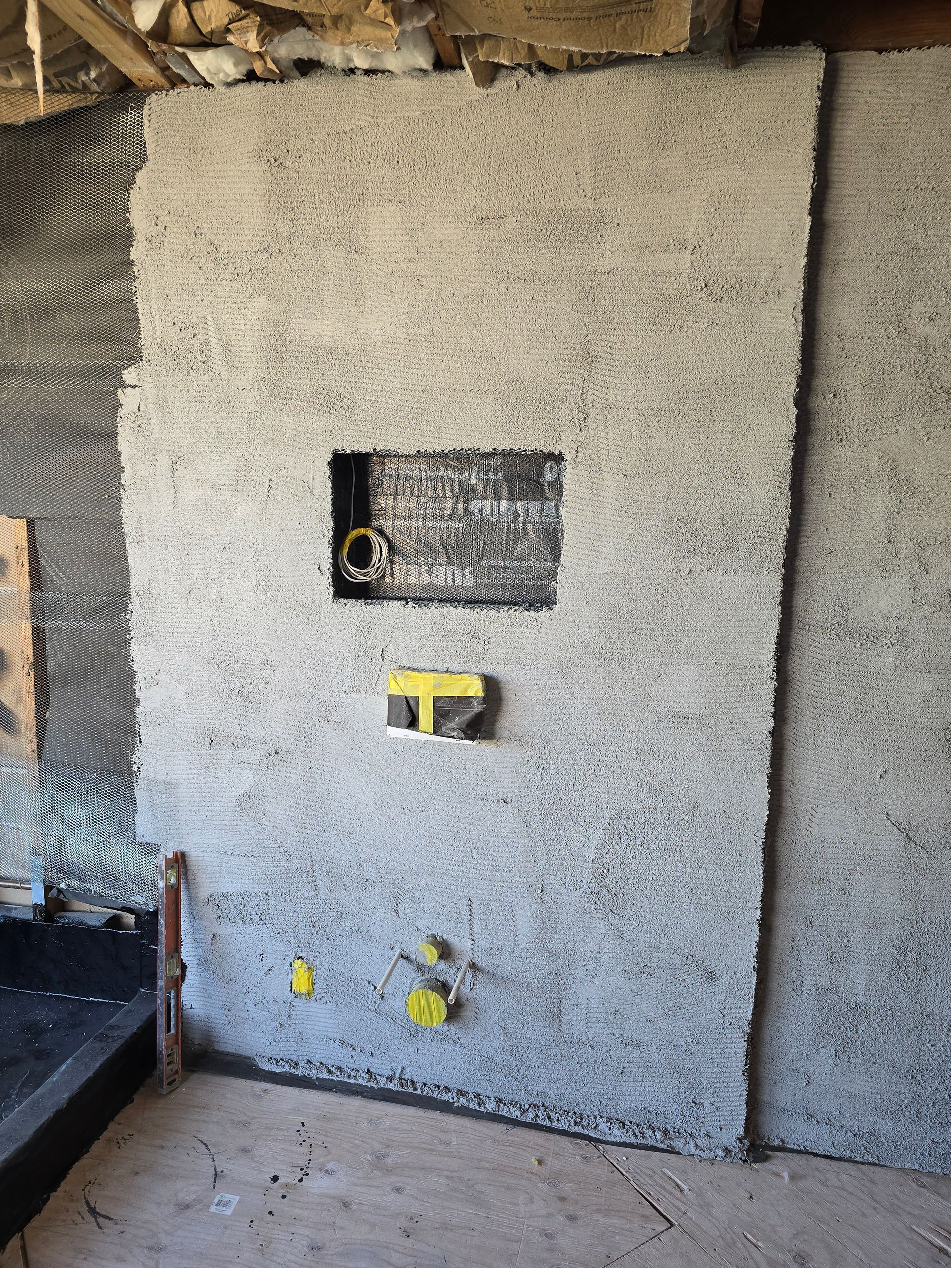 Unfinished interior wall with plumbing and electrical openings, gray textured surface, and concrete floor