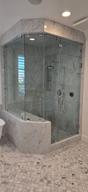Glass corner shower with gray marble tile and mosaic floor in a bright bathroom