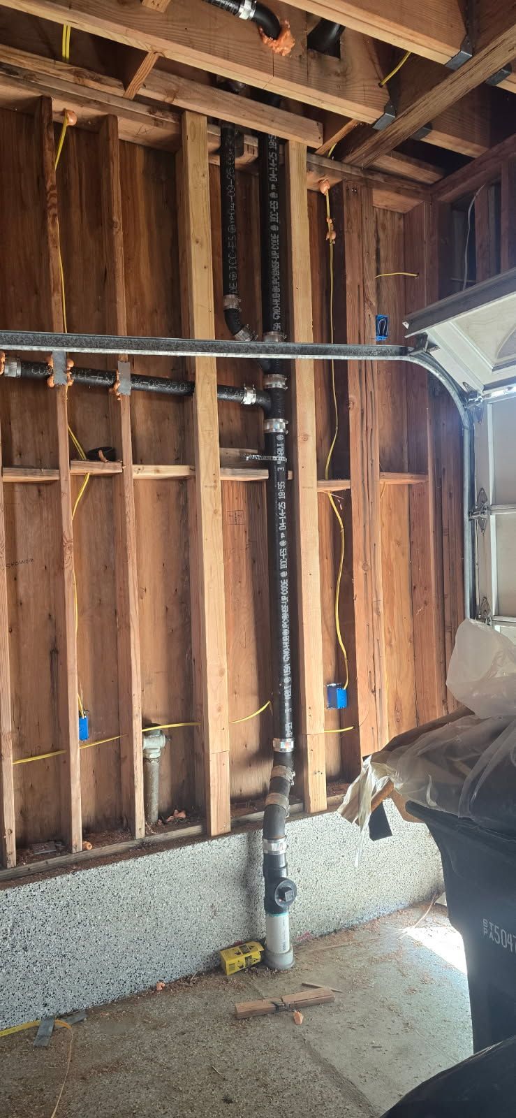 Unfinished garage wall with exposed studs, a vertical pipe, and a vent duct on the right.