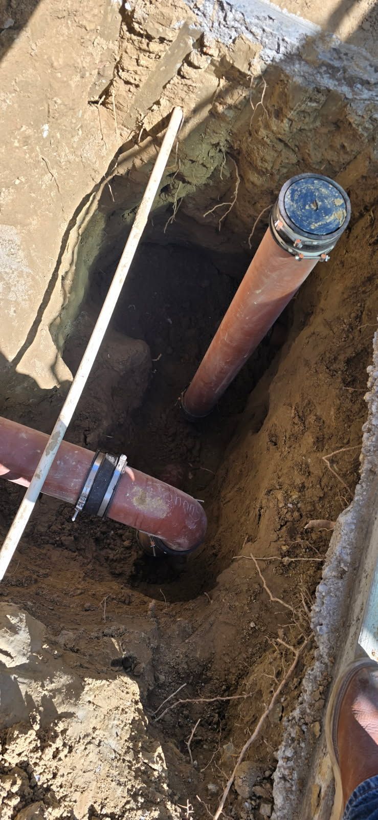 Open trench with exposed red pipes and a capped vertical pipe in dirt ground