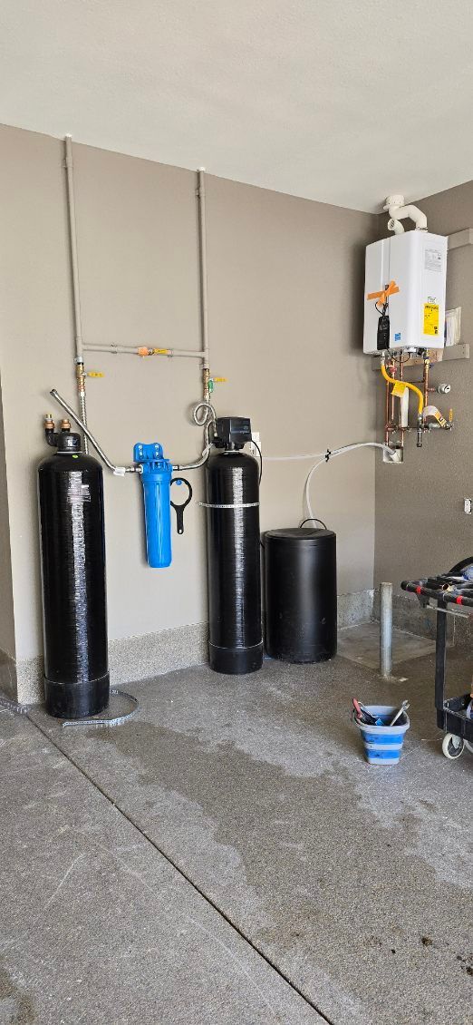 Utility room with water softener tanks, filter system, and wall-mounted heater on a concrete floor