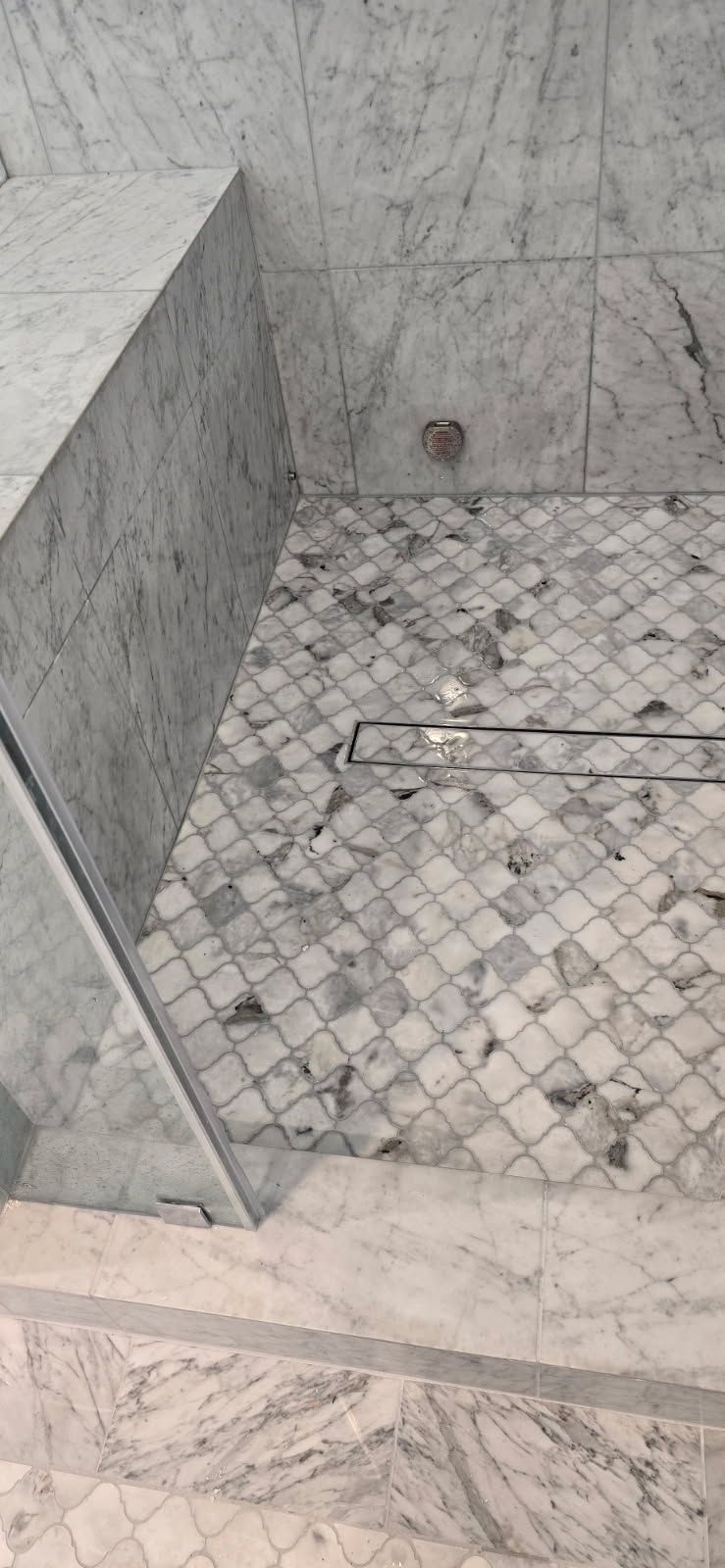 Marble-tiled bathroom shower area with a small floor drain and partition wall