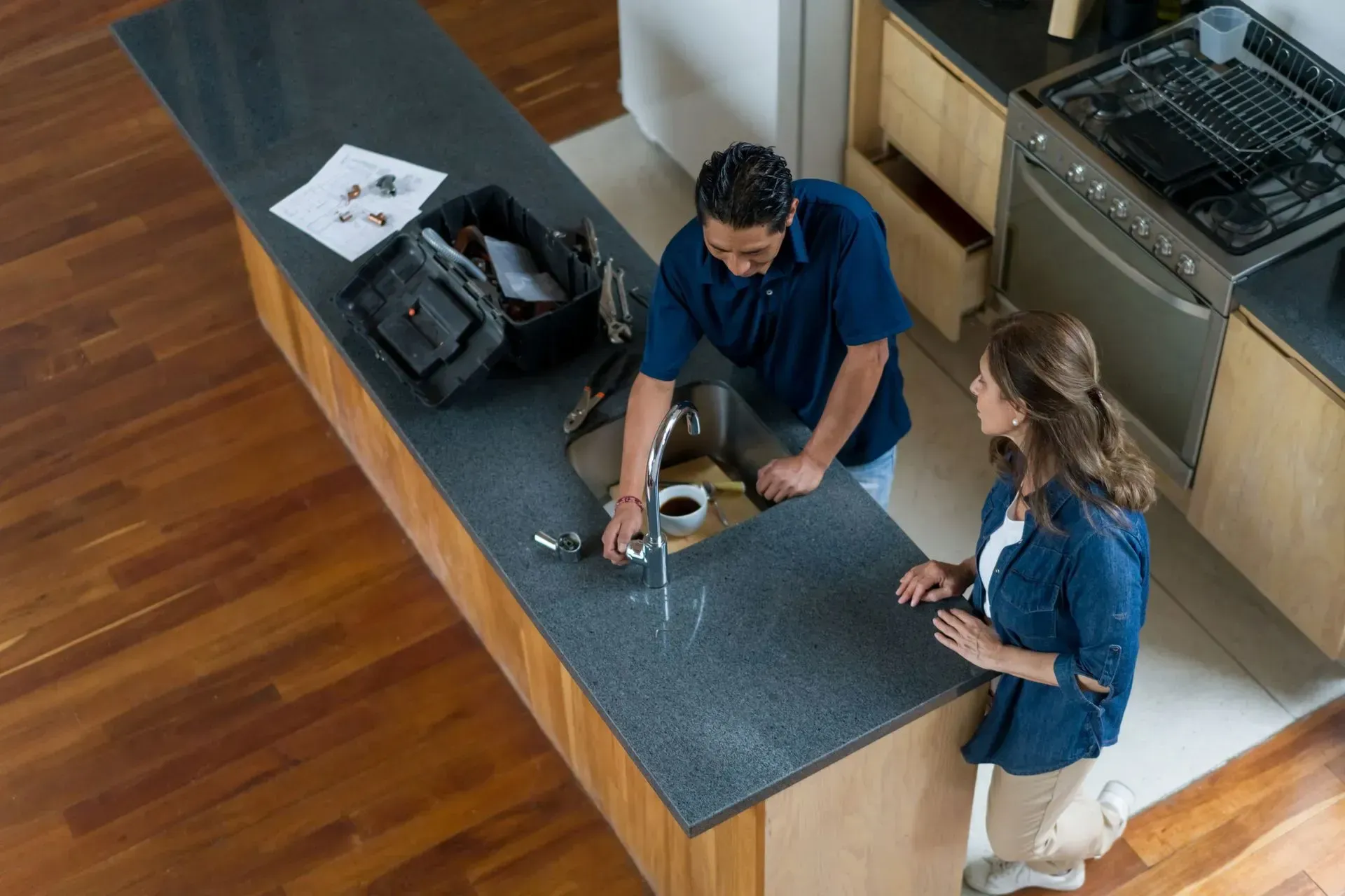 Two people standing at a kitchen island, handling a small device on a blue mat.