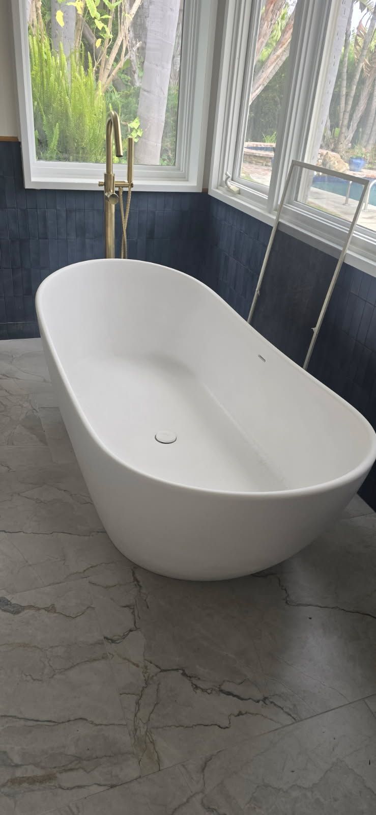 Modern white freestanding bathtub in a bright bathroom with gray marble tile flooring.