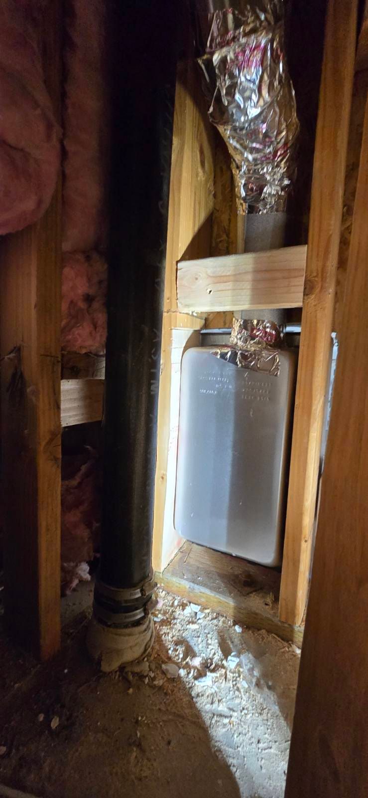 Exposed wall cavity with ductwork and a rectangular HVAC unit framed by wooden studs and insulation debris.