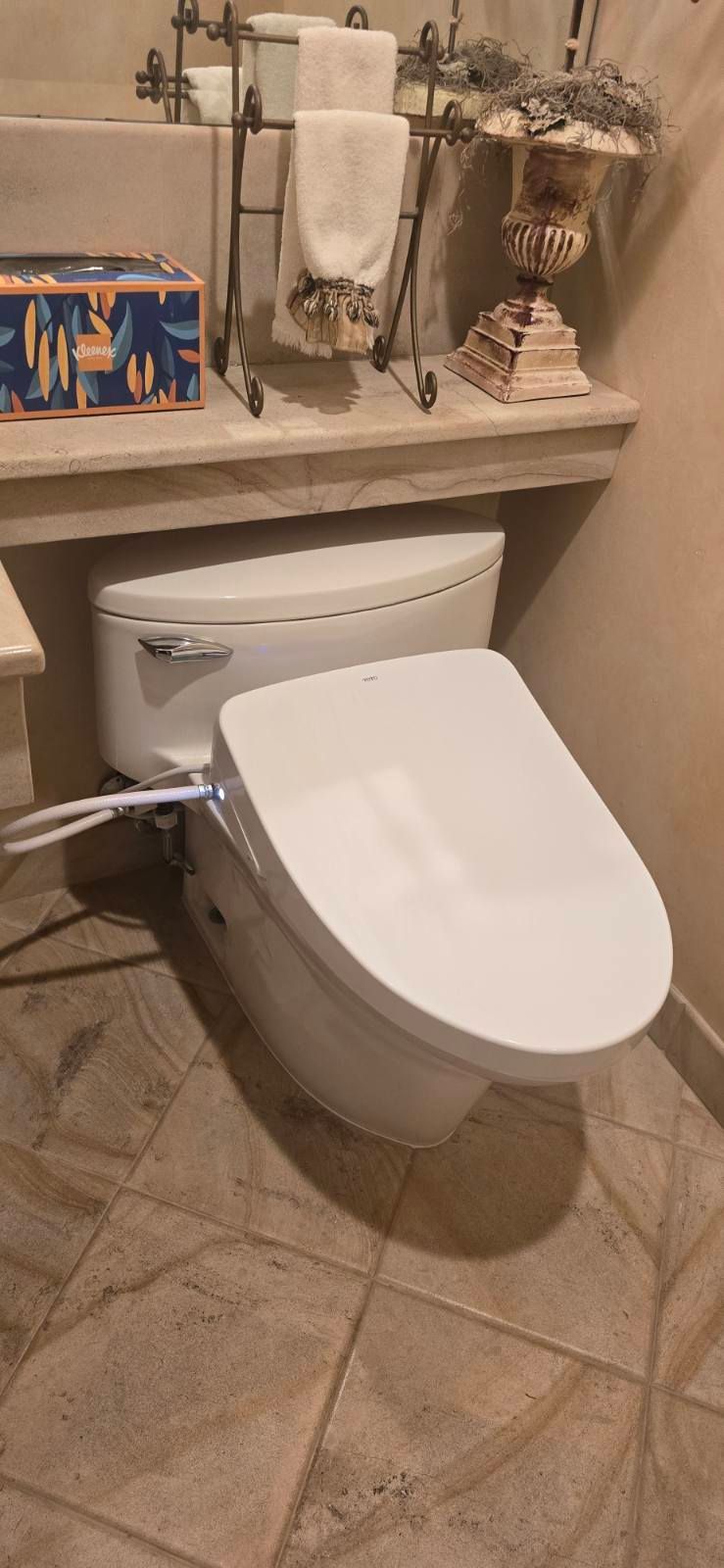 Bathroom with a toilet, tiled floor, and decorative shelf above it.