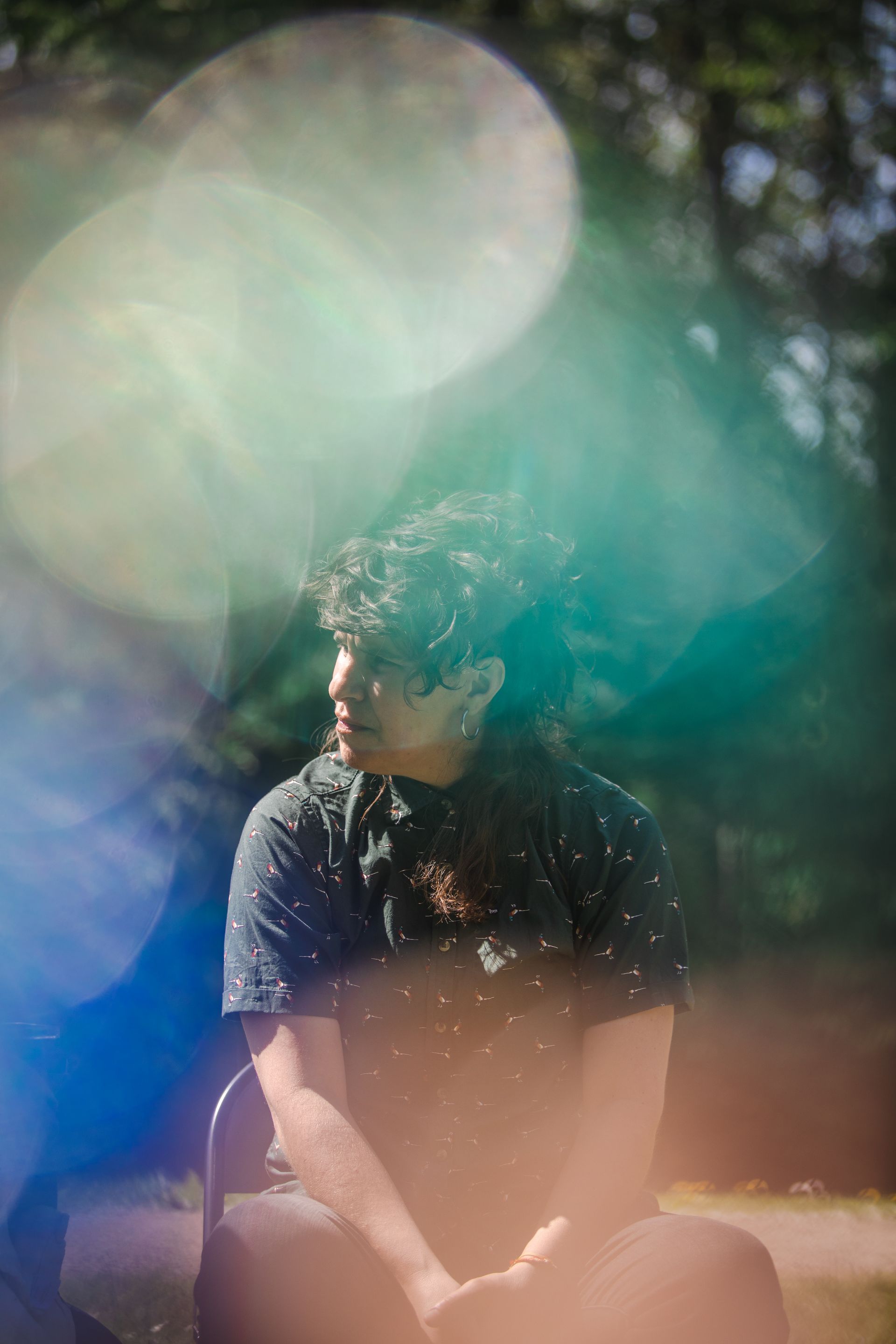 A person sitting outdoors, blurred by colorful lens flare.