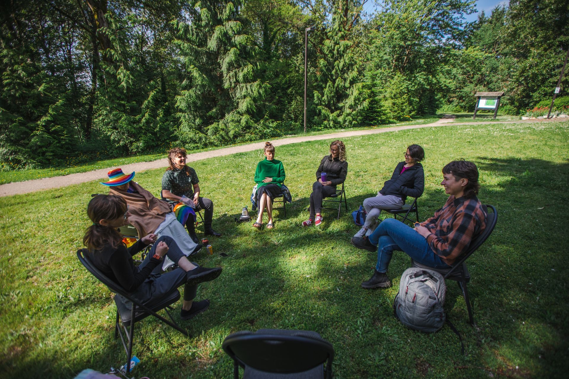 A group of people are sitting in a circle on the grass in a park.