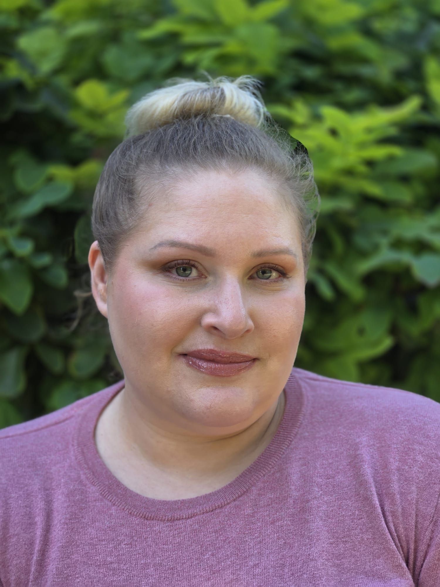 Portrait of a smiling person in a purple sweater against a leafy green background