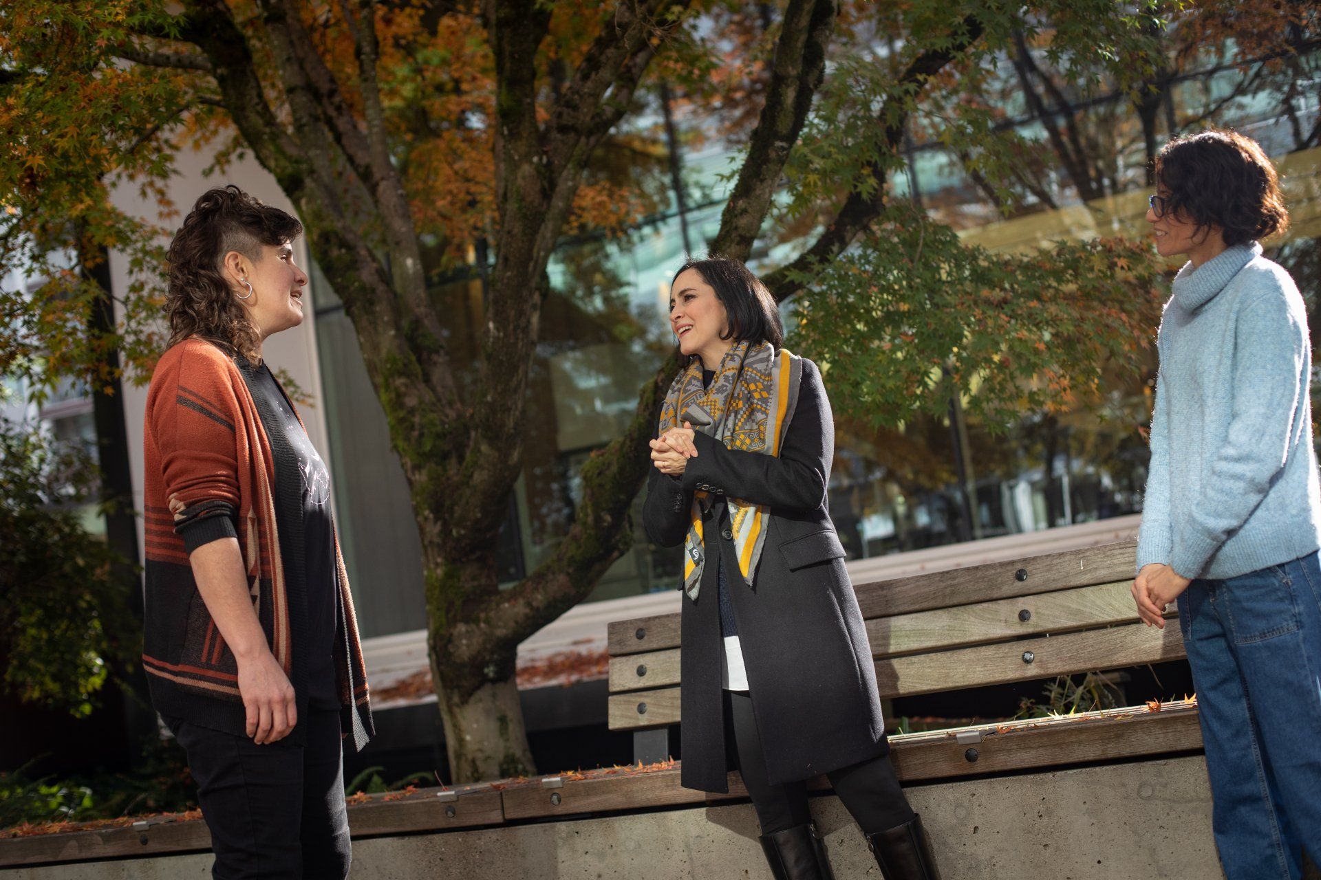 Three persons are standing next to each other in front of a tree.