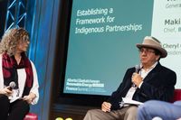 Two people sit on a stage during a panel titled 