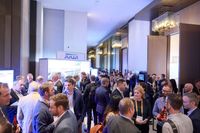 A crowded indoor networking event at a brightly lit conference hall with professional attendees socializing and talking.