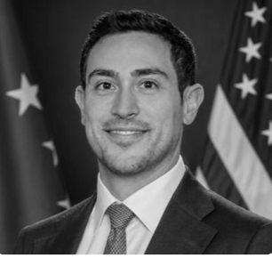 Man in suit and glasses looking to the side with a slight smirk.