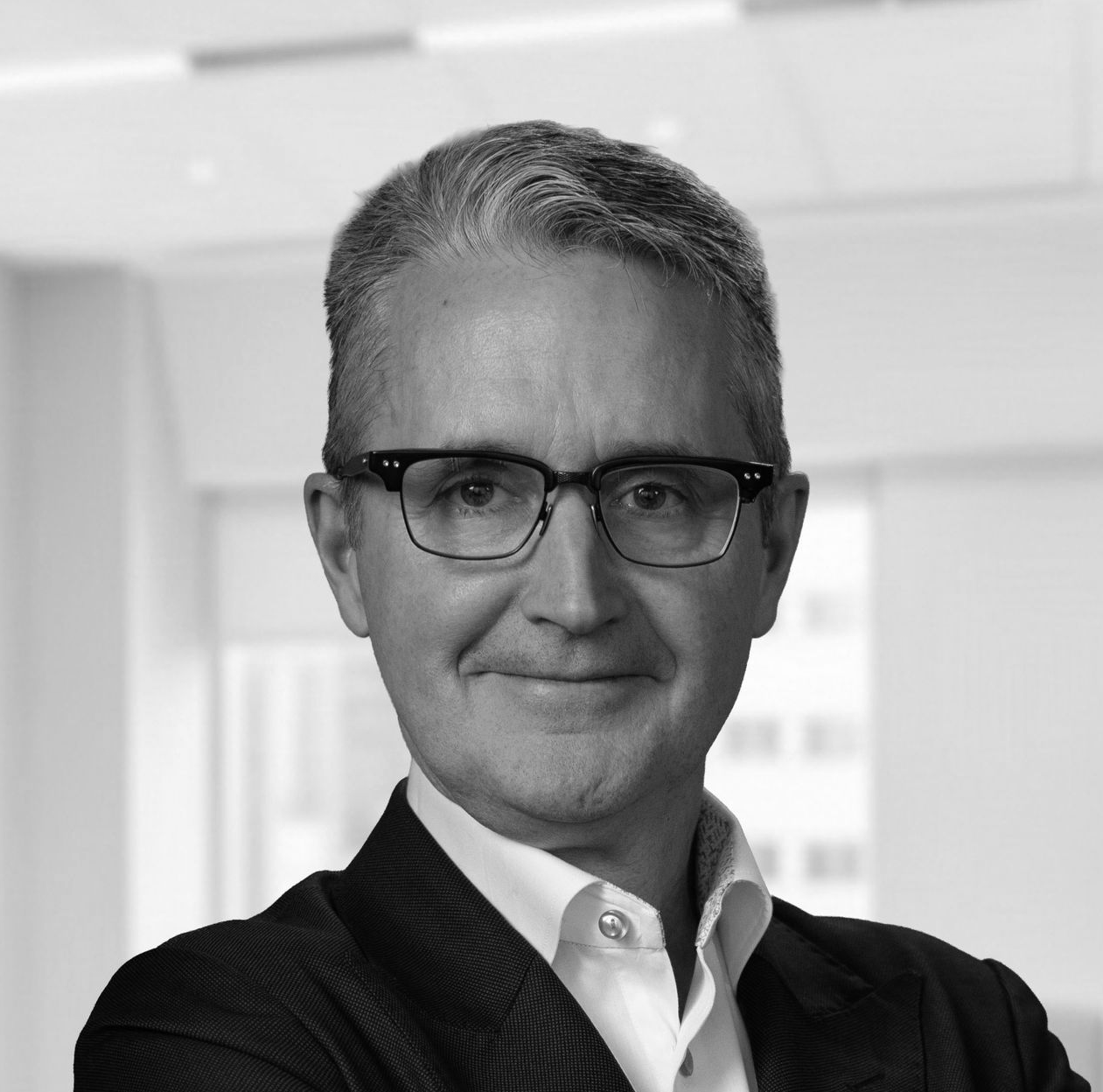 Man in suit and glasses looking to the side with a slight smirk.