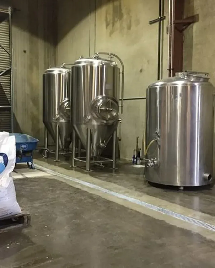 A row of stainless steel tanks are lined up in a brewery.