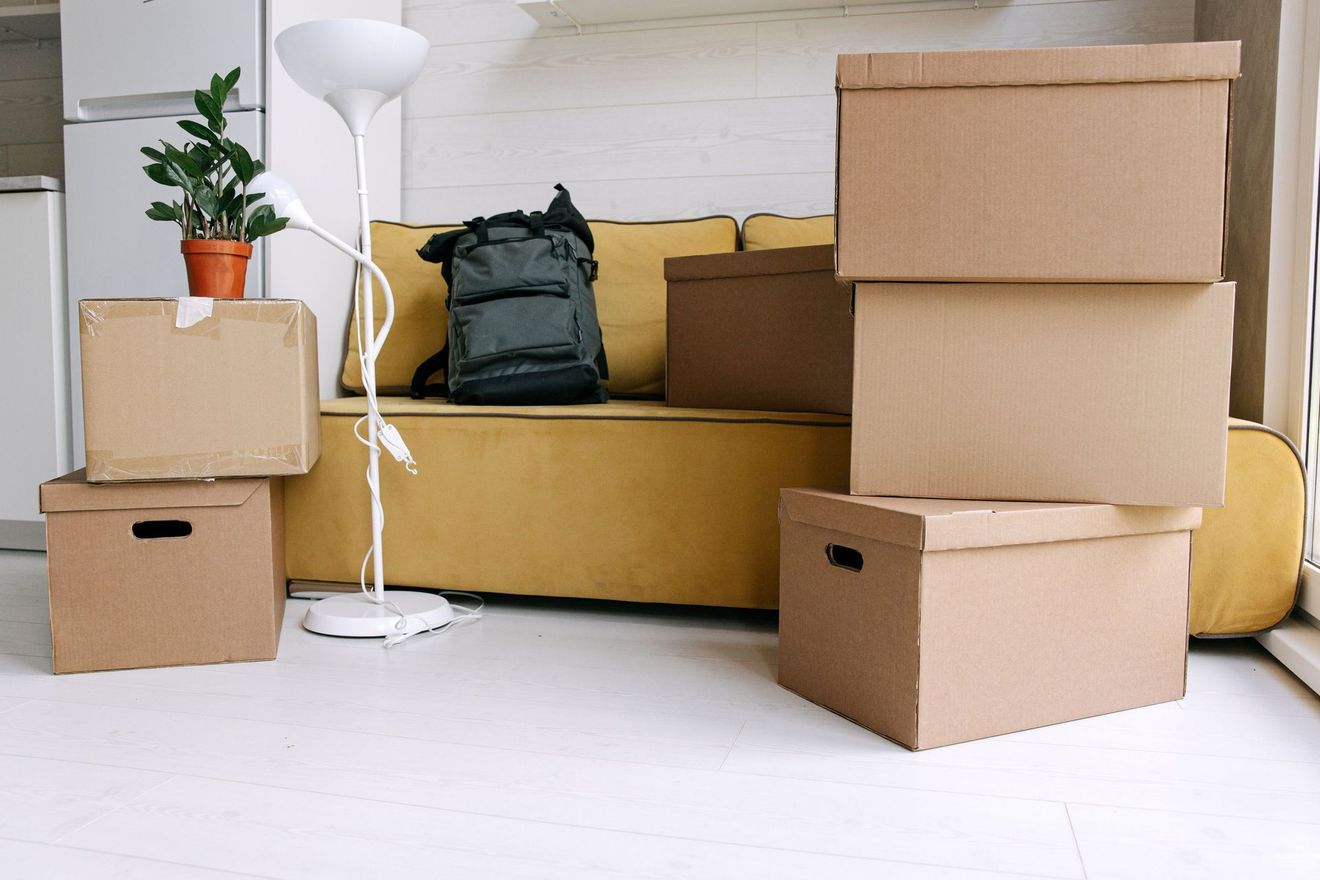 Moving boxes and a backpack arranged in a bright room with a white floor and floor lamp