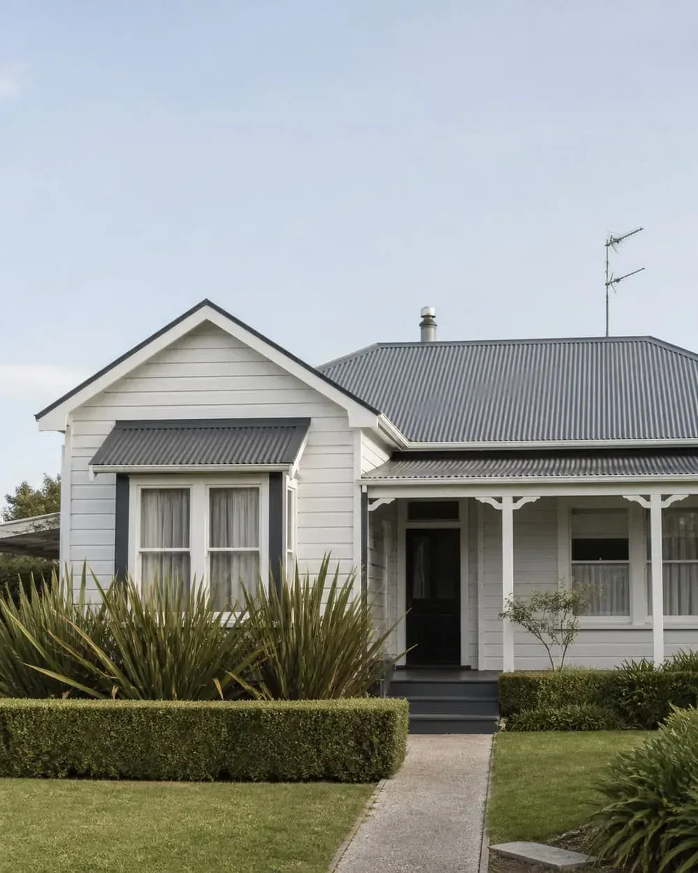 White house with gray roof, front porch, and hedge-lined walkway