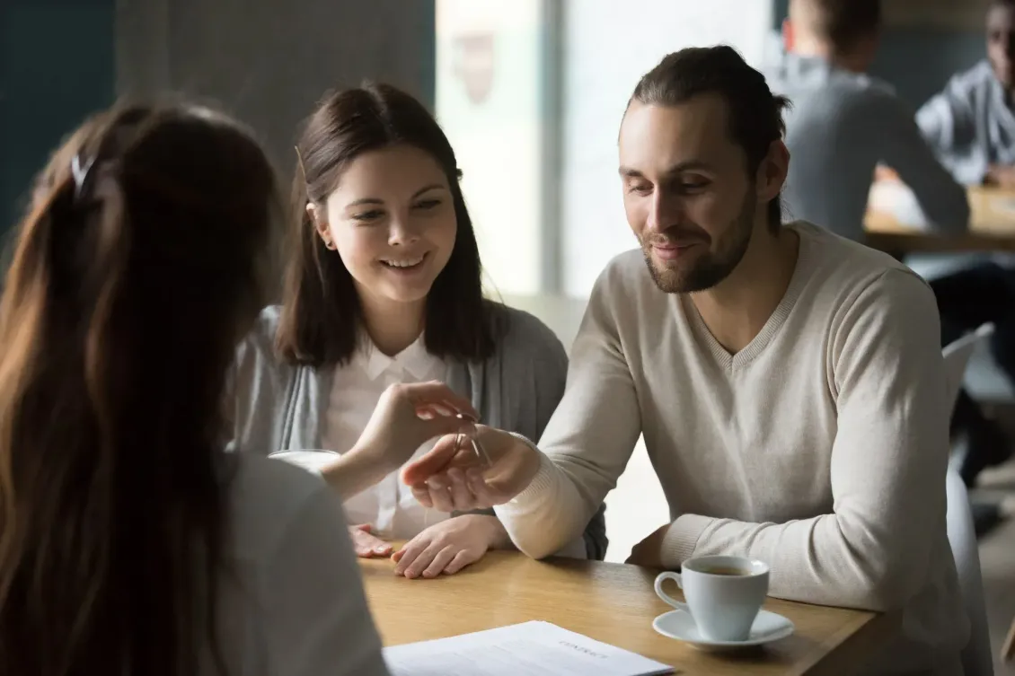 Three people talking at a café table, smiling with coffee cups and papers.