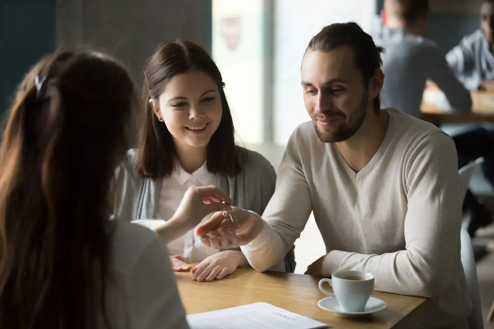 Three people talking at a café table, smiling with coffee cups and papers.