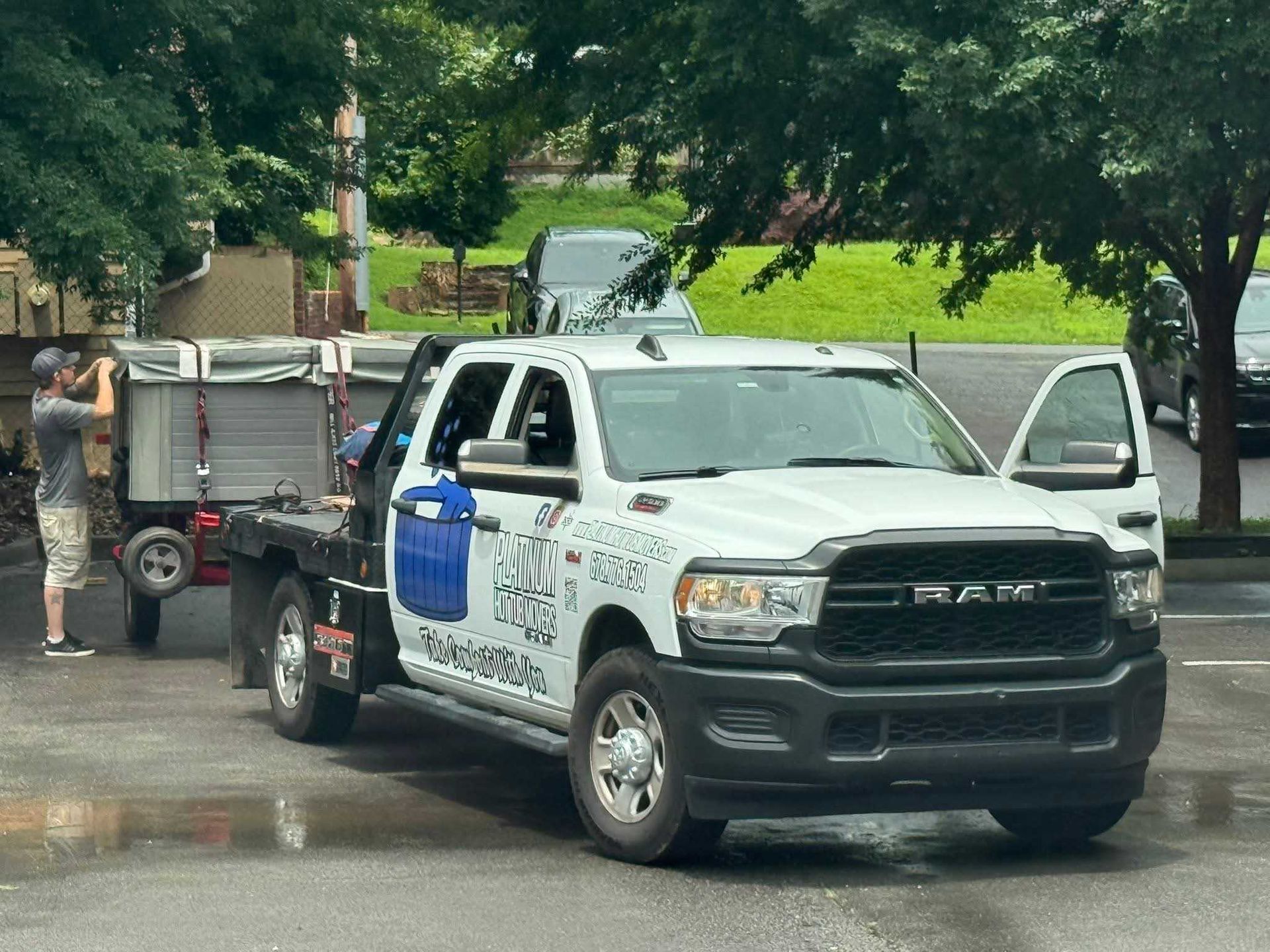 White RAM truck with trailer, parked outdoors. A man stands by the trailer, appearing to adjust something. The truck's door is open.