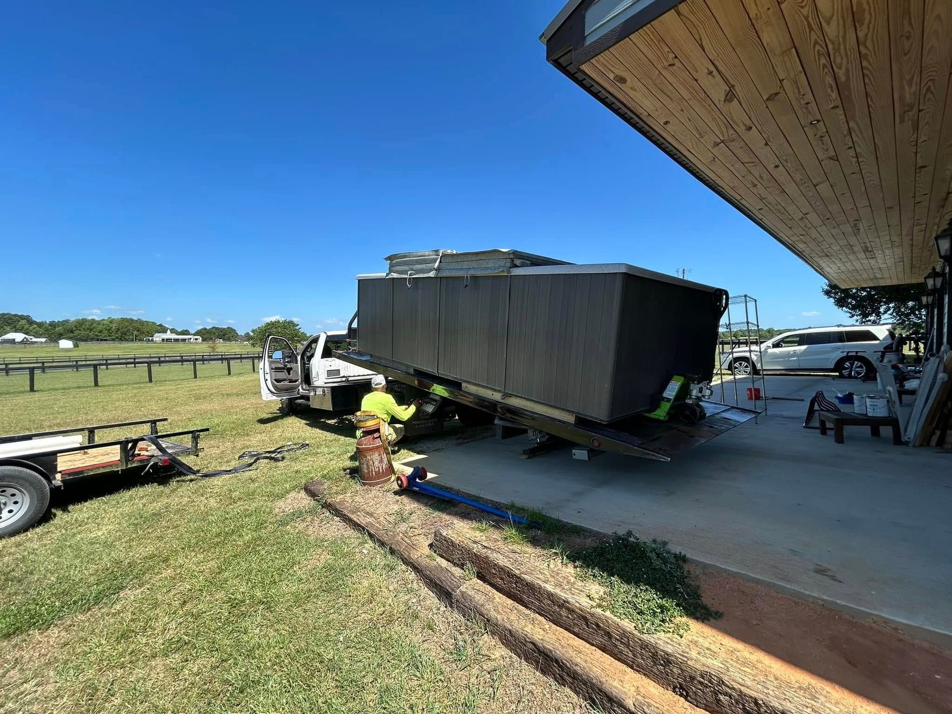 Truck unloading a large, black rectangular object near a building. A person in a safety vest is assisting.