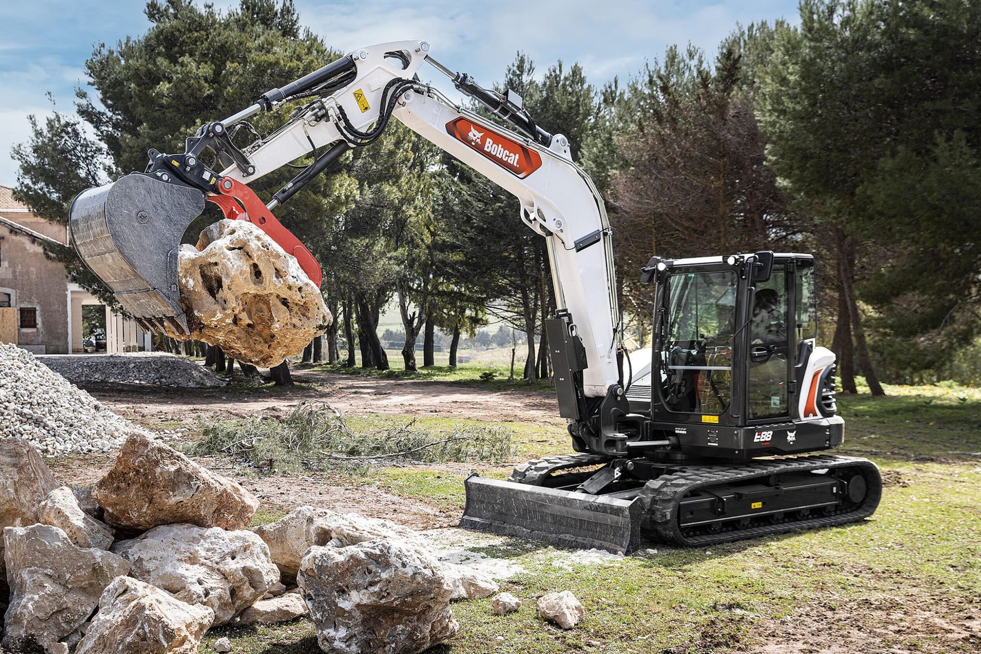 Un escavatore Bobcat bianco e nero solleva una grande roccia in una zona erbosa.