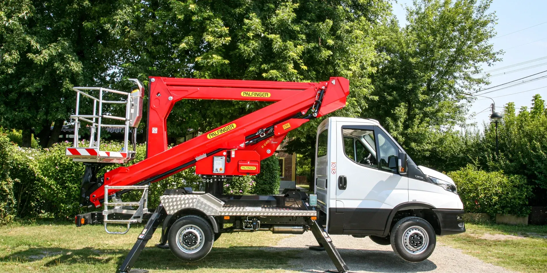 Piattaforma aerea rossa montata su un camion bianco, parcheggiata sull'erba.