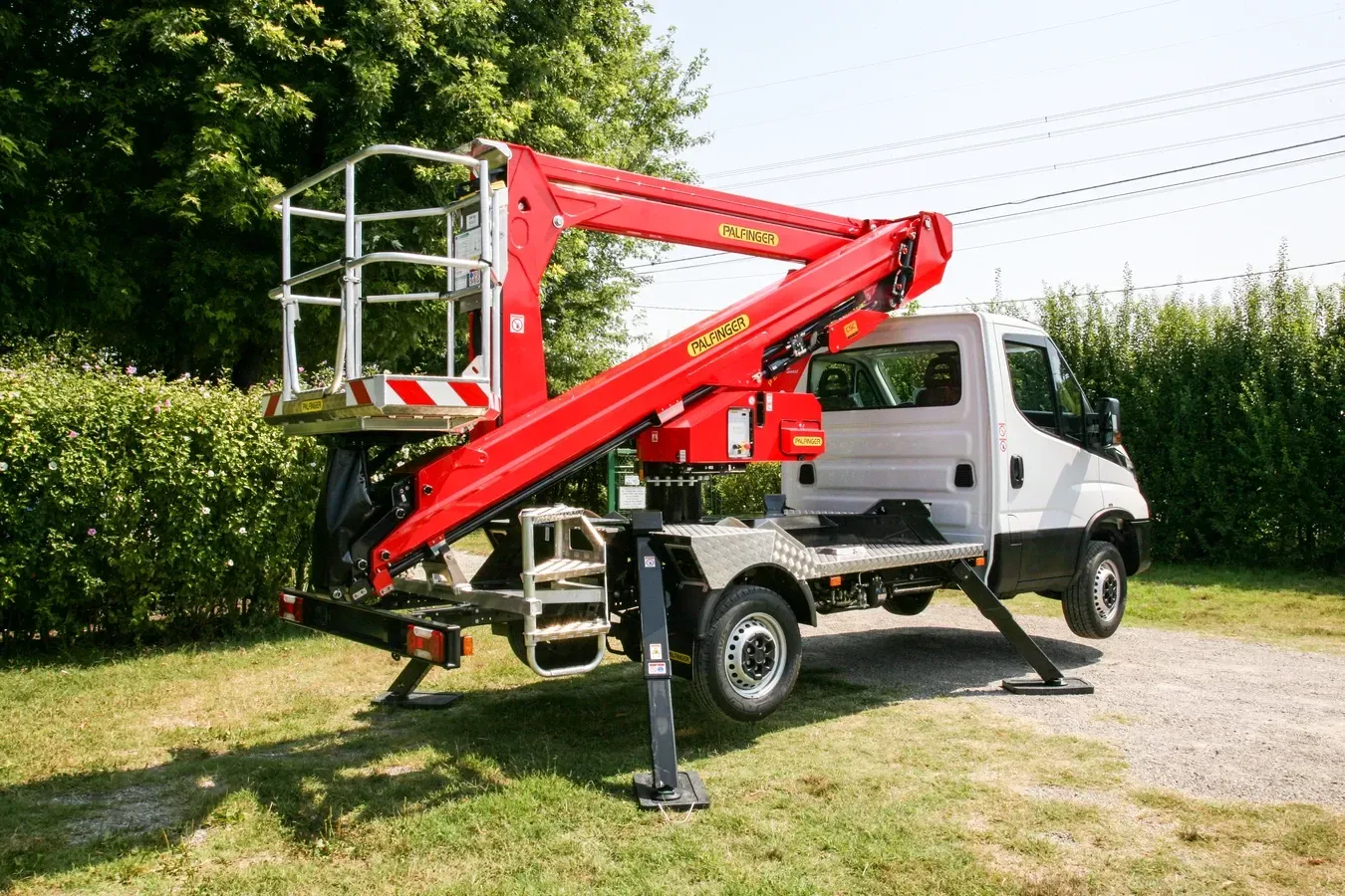 Piattaforma aerea rossa montata su un camion bianco, parcheggiata sull'erba.