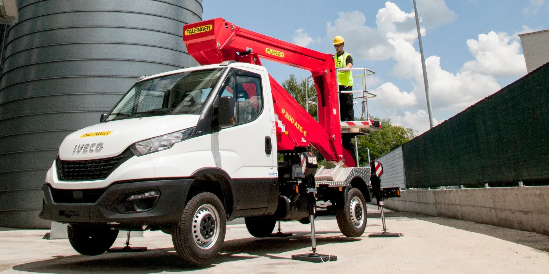 Camion bianco e nero con un sollevatore rosso su cui è caricata una persona che indossa un giubbotto di sicurezza giallo.