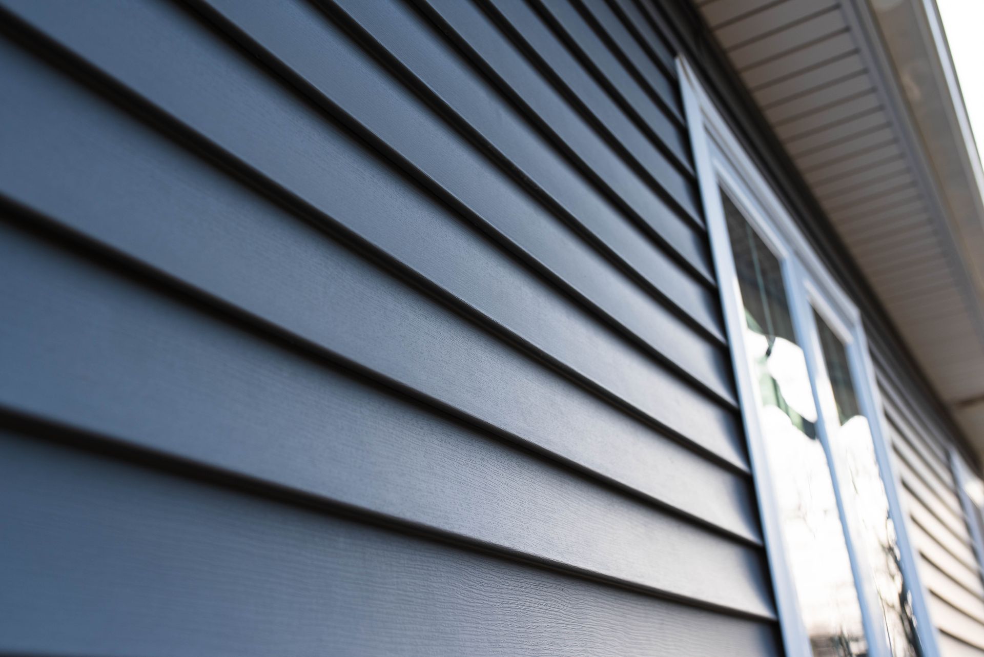 A close-up view of dark blue horizontal vinyl siding on the exterior of a house, featuring a white-trimmed window.