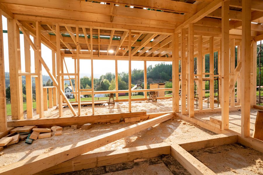 Wooden framing of a house under construction, showing open studs and rafters overlooking a grassy landscape.