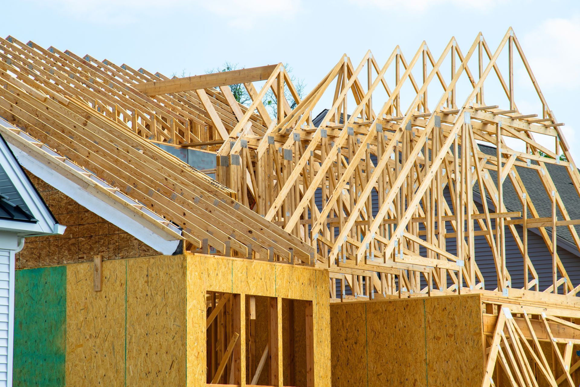 The wooden frame of a house under construction, showing roof trusses and OSB sheathing against a blue sky.