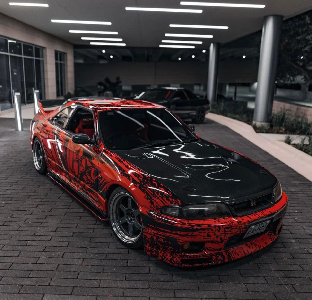 A red and black car is parked in a parking lot