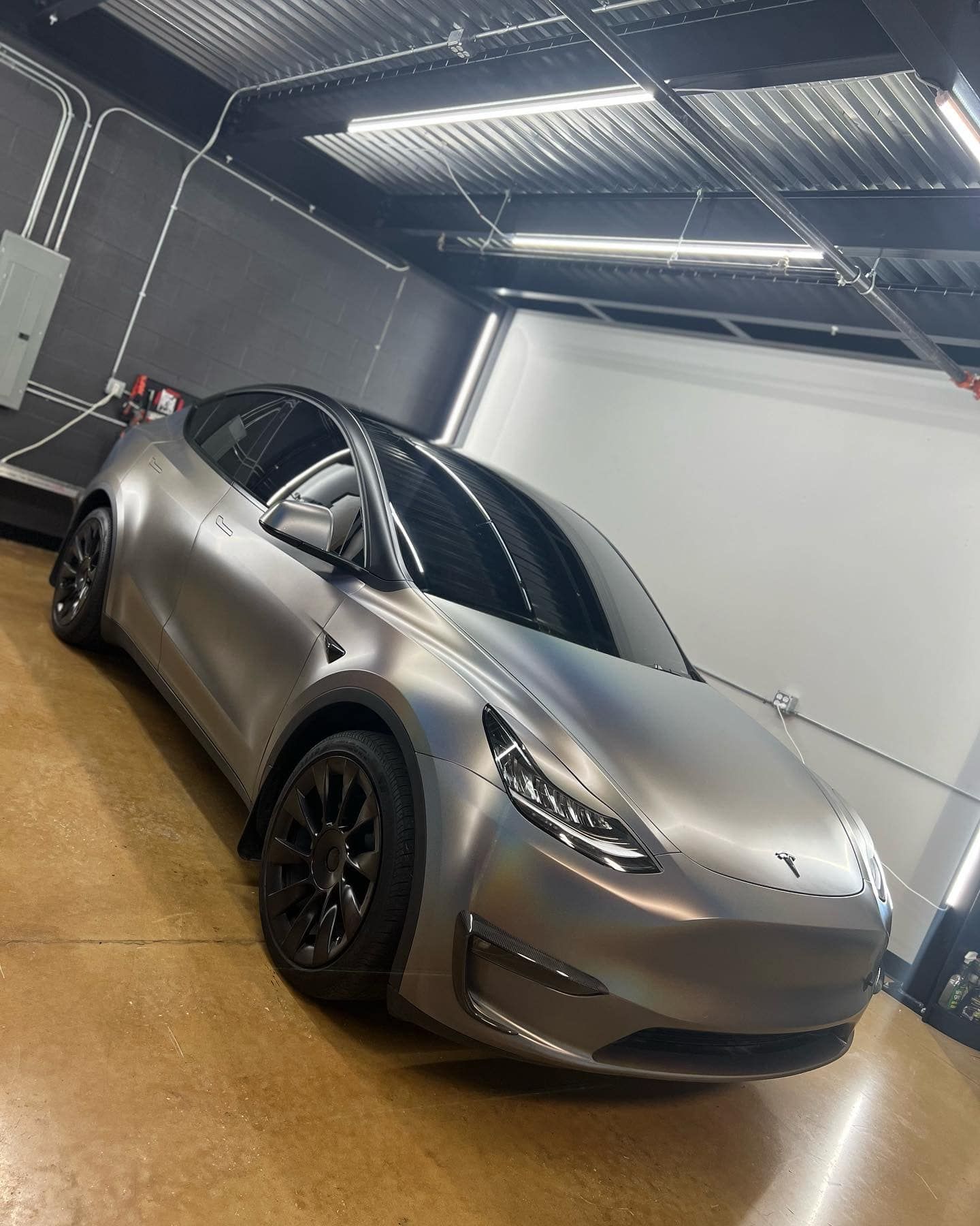 A silver tesla model y is parked in a garage.