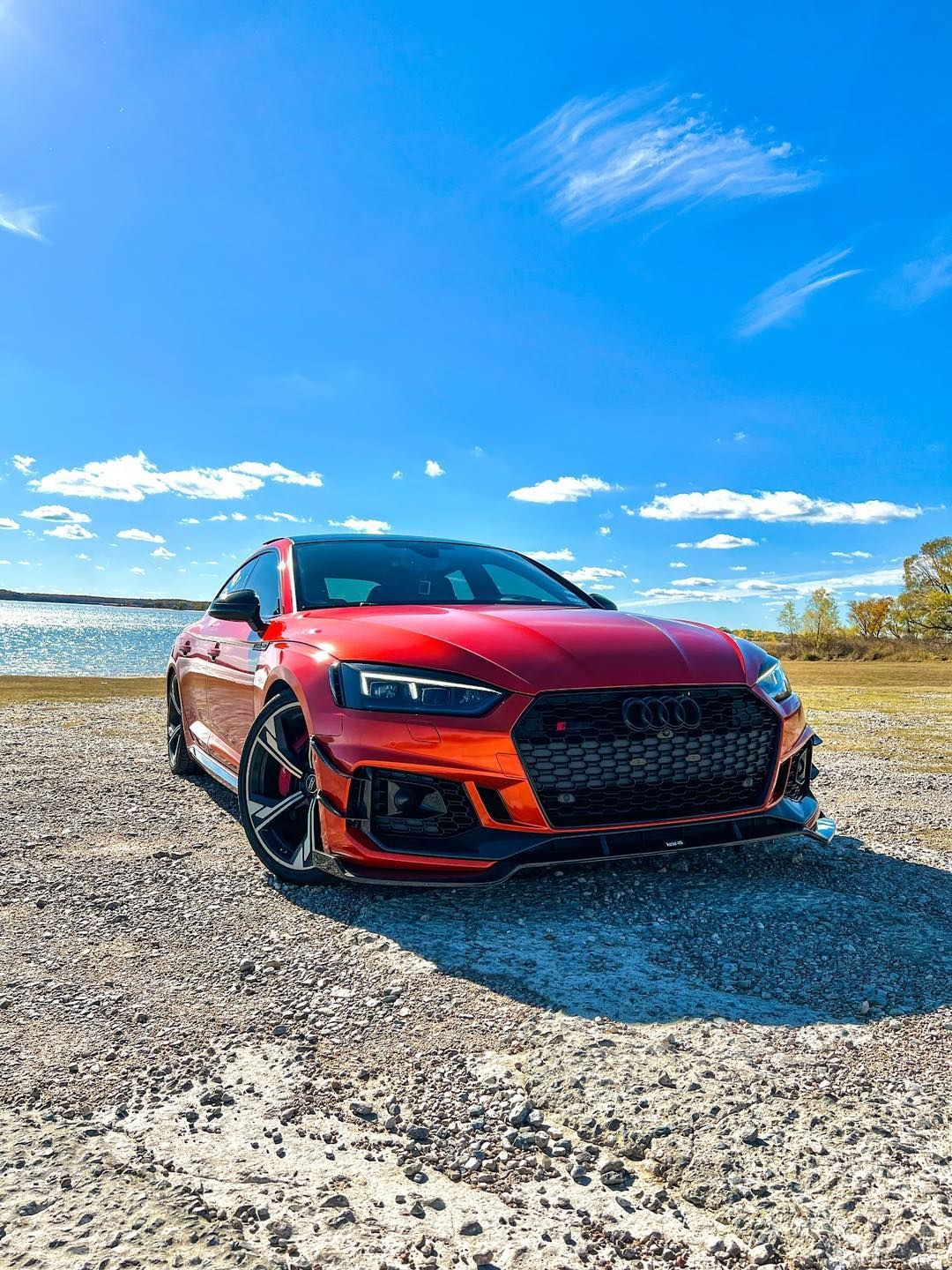 A red audi a5 is parked on a dirt road next to a body of water.
