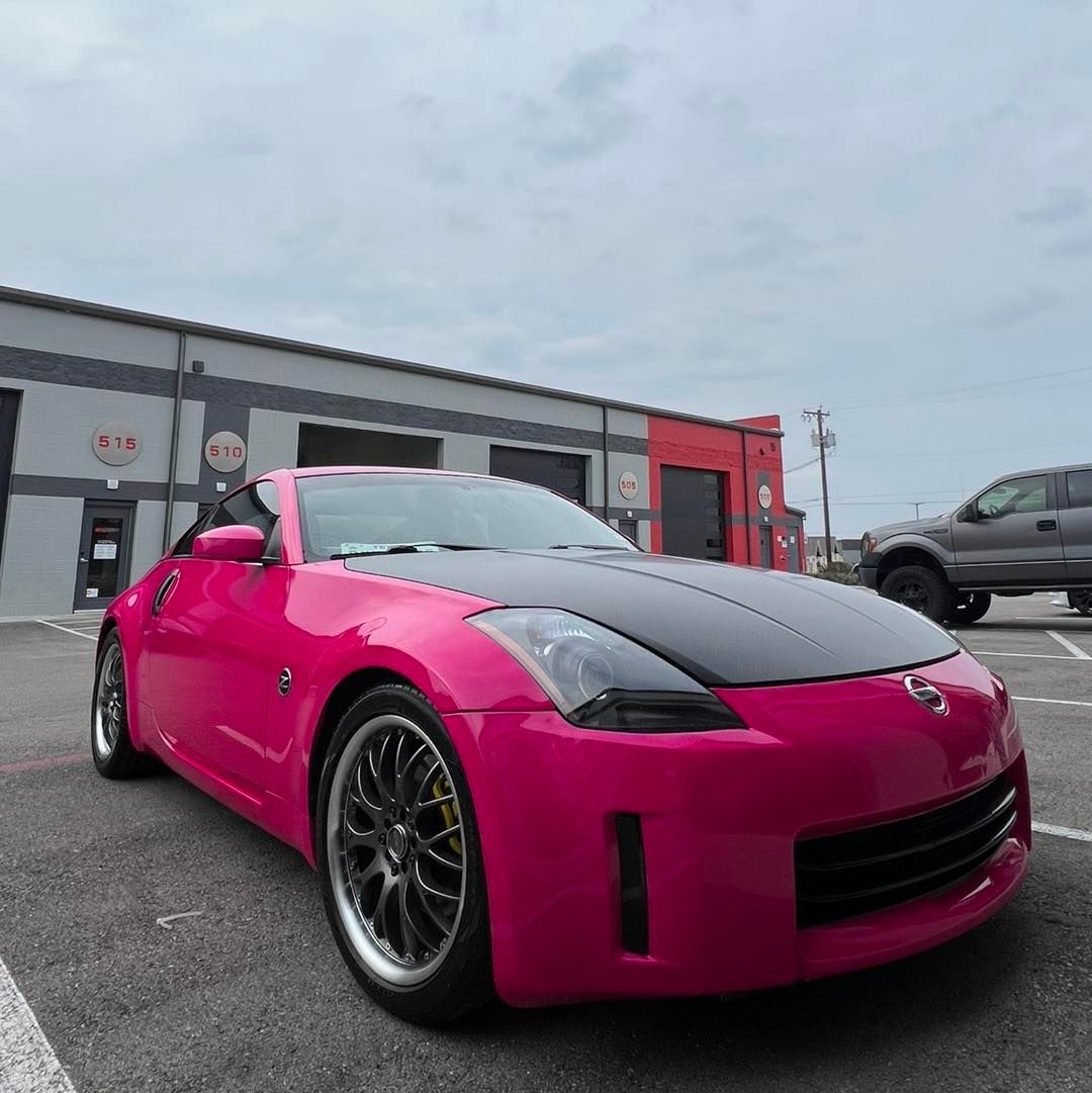 A pink car with a black hood is parked in a parking lot
