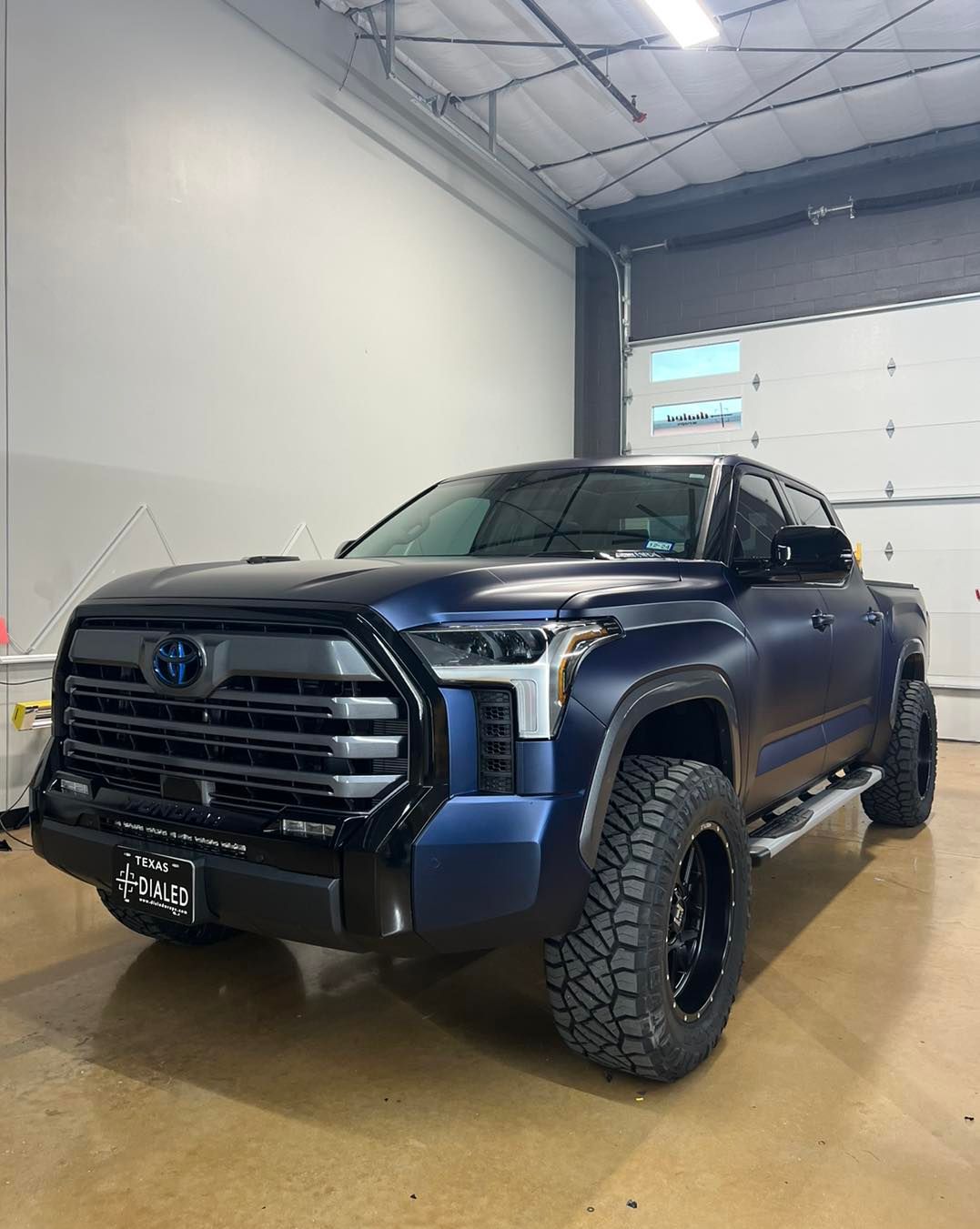 A blue truck is parked in a garage next to a garage door.