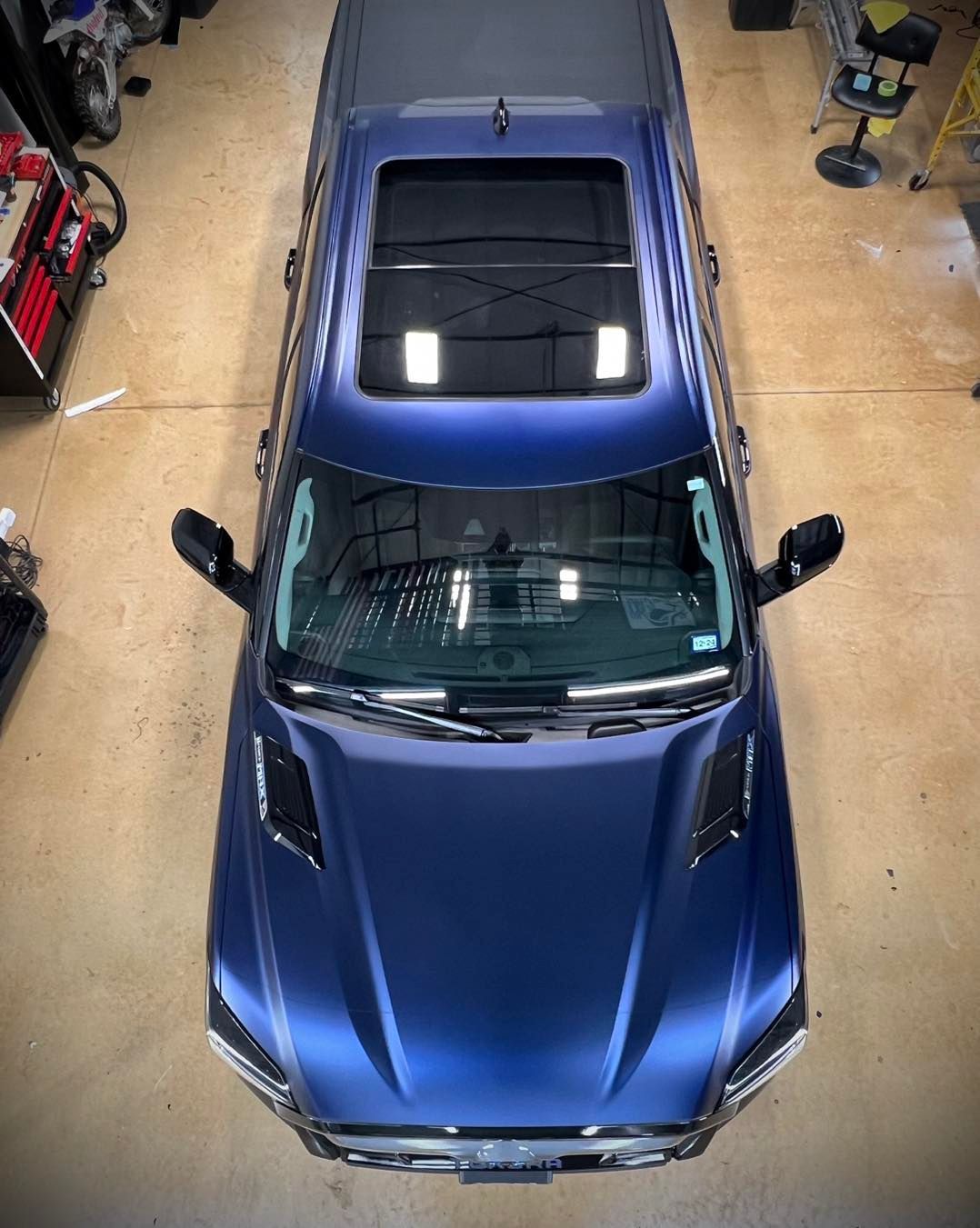 A blue car with a sunroof is parked in a garage