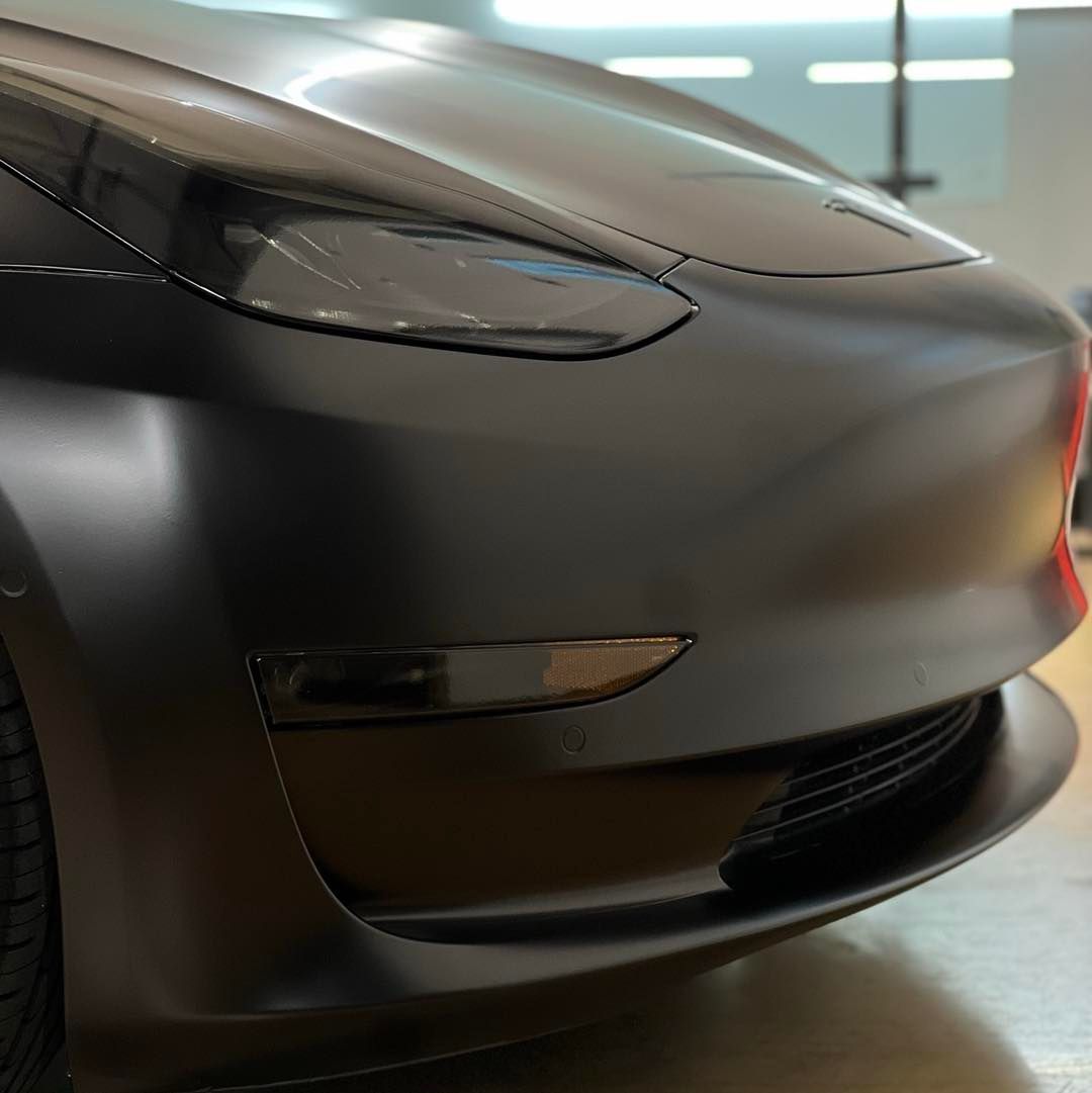 A black tesla model 3 is parked in a garage.
