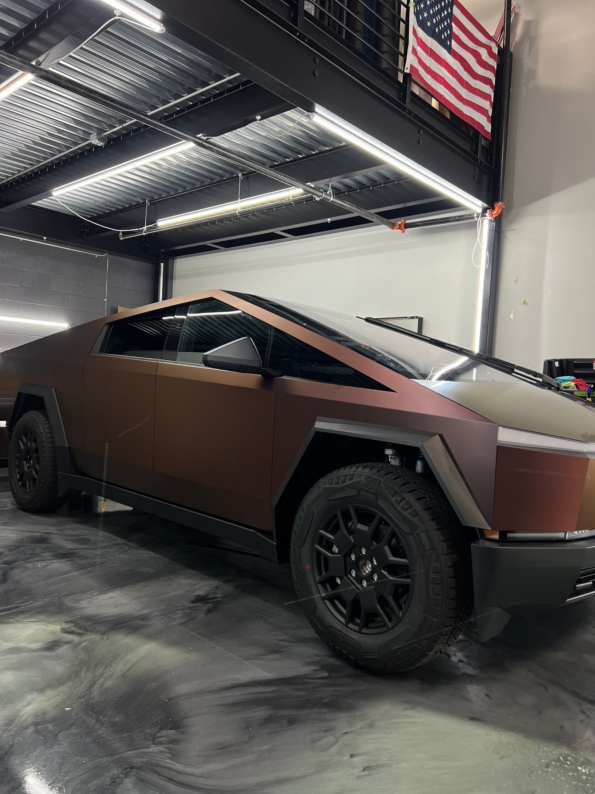 A tesla cybertruck is parked in a garage next to an american flag.