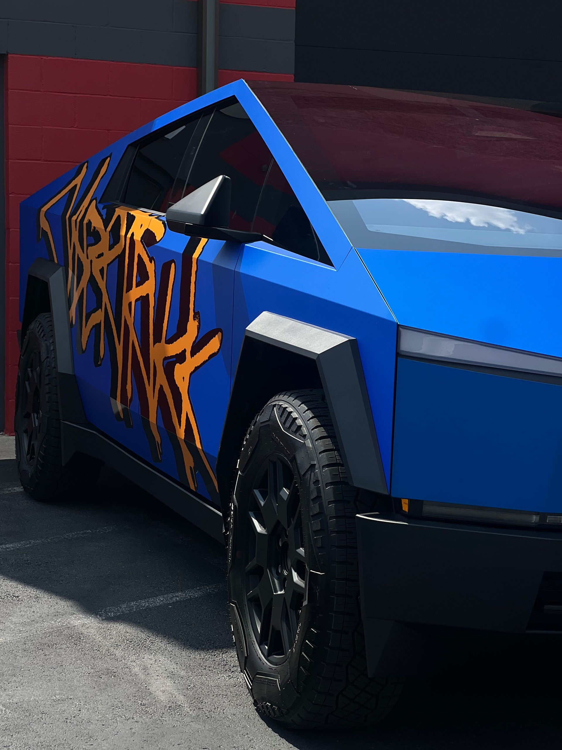 A blue car with graffiti on the side is parked in front of a building.