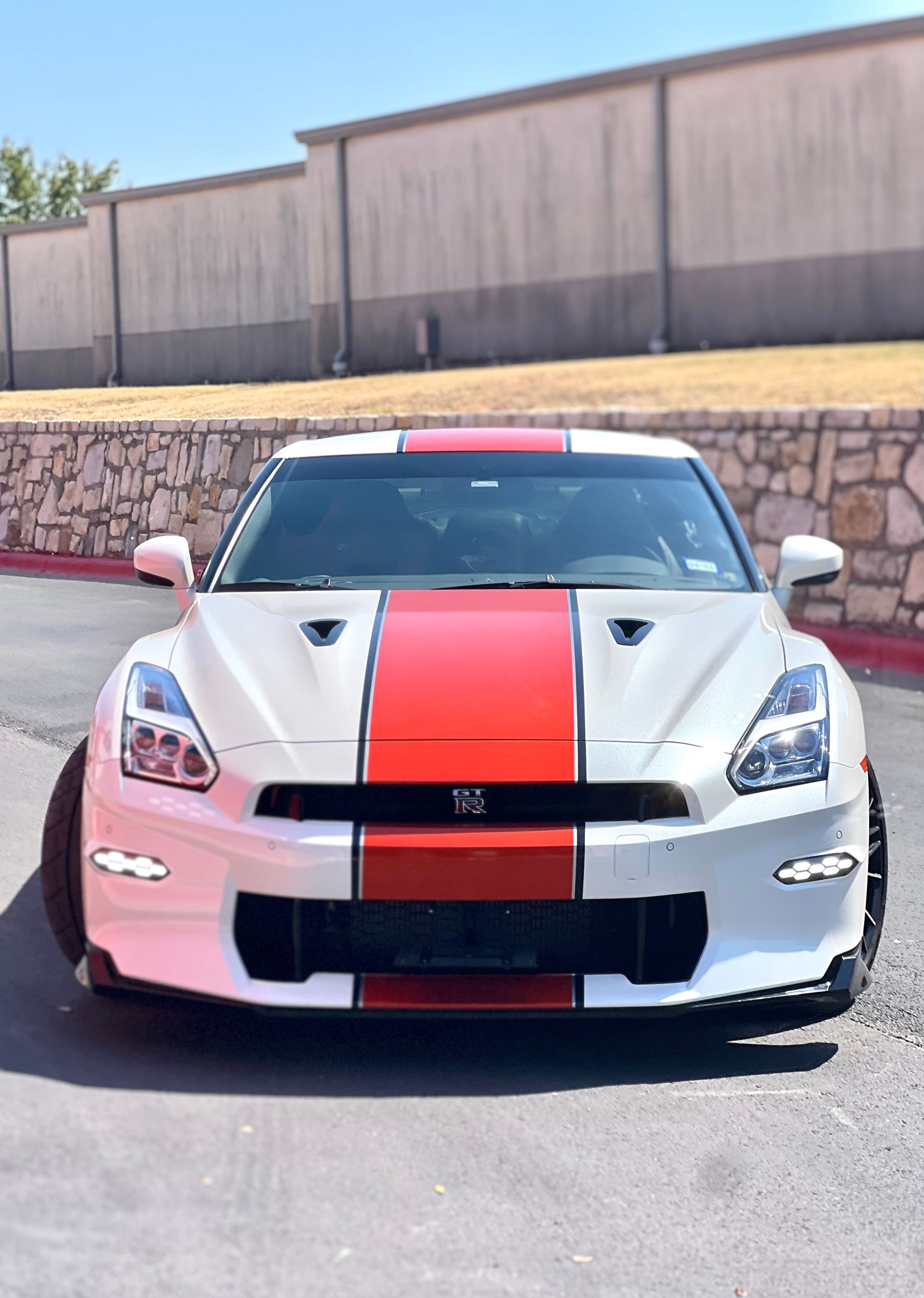 A white sports car with red stripes on the front is parked in a parking lot