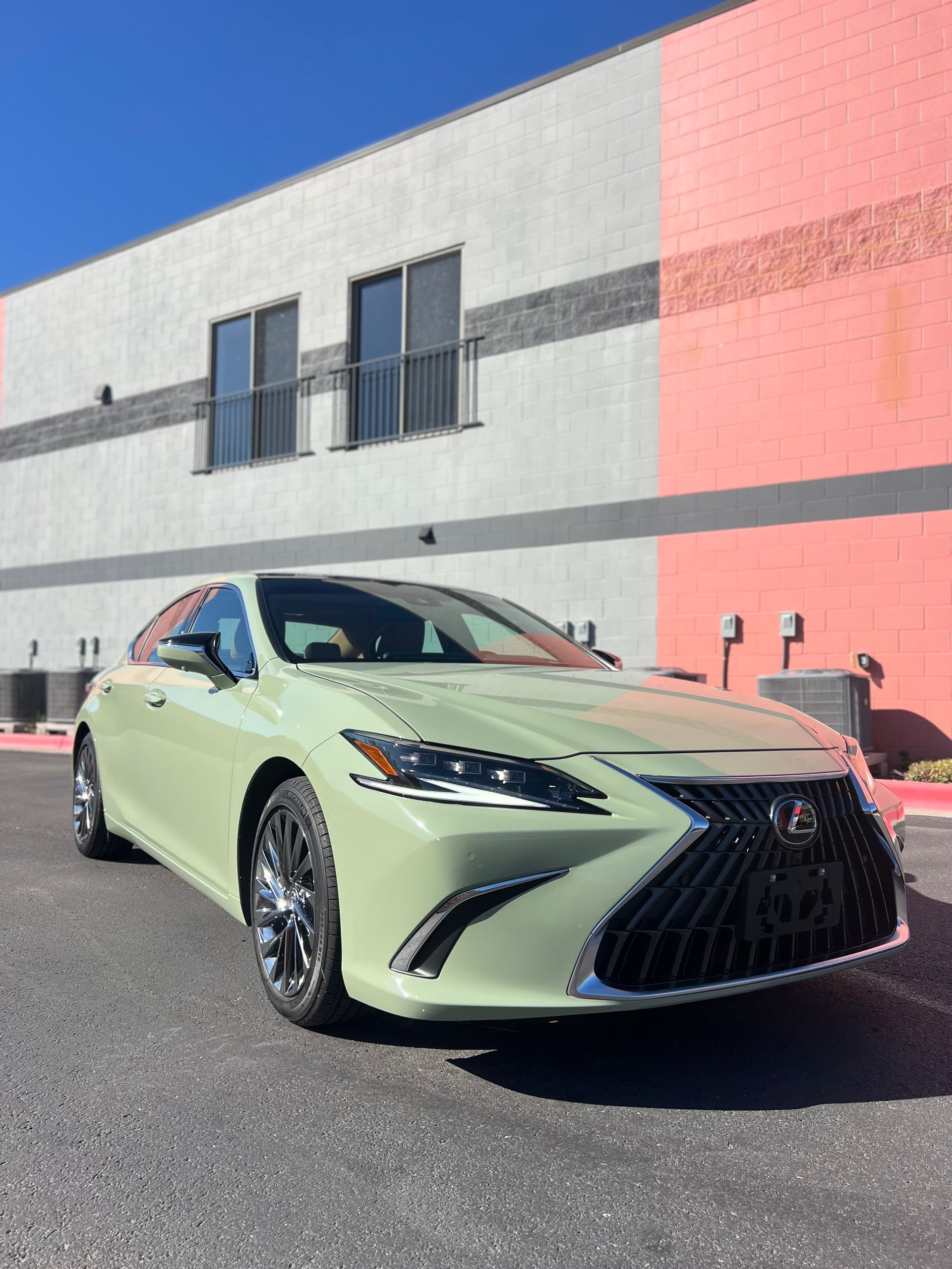 A green lexus is parked in front of a building.