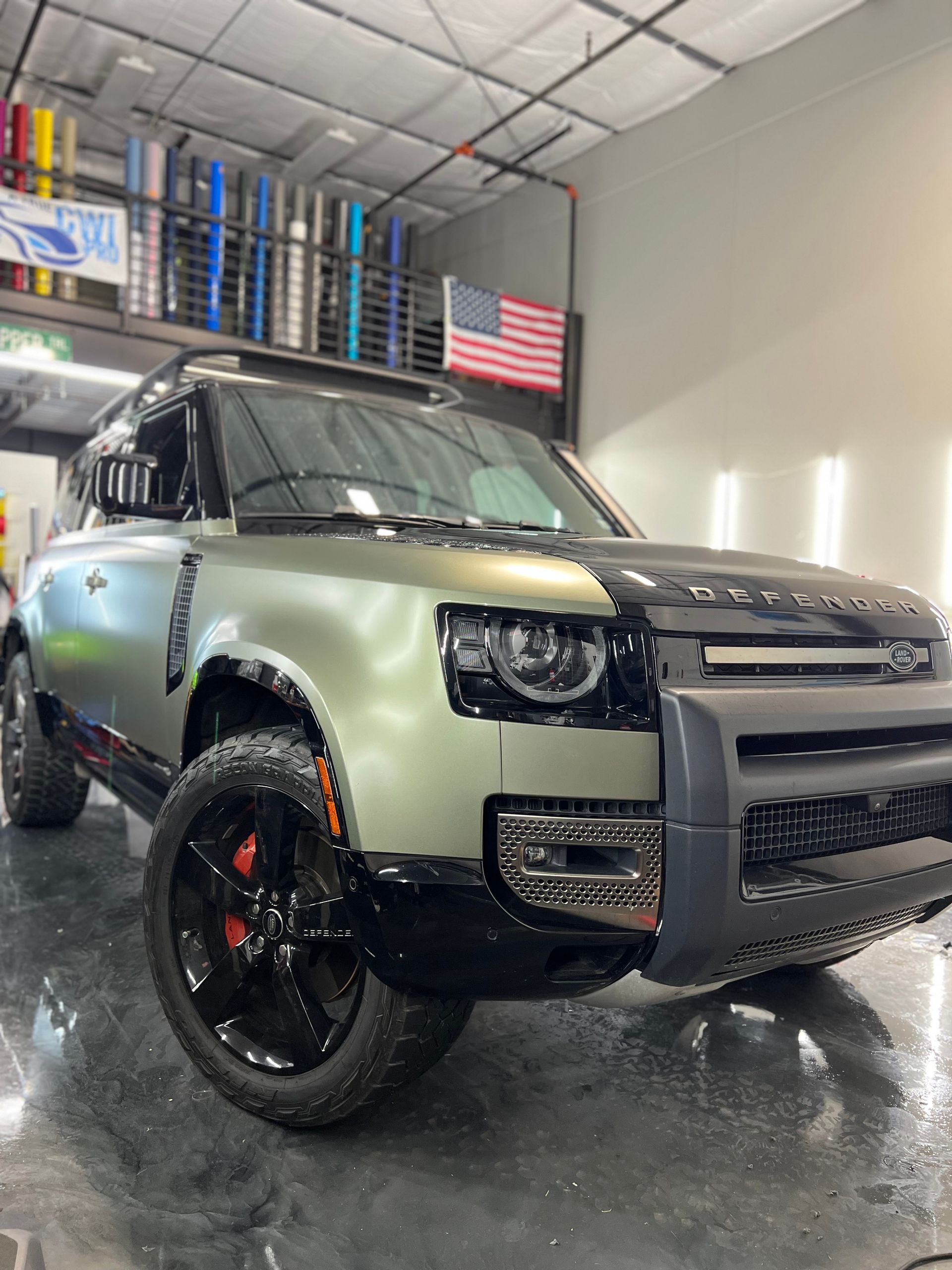 A green land rover defender is parked in a garage.