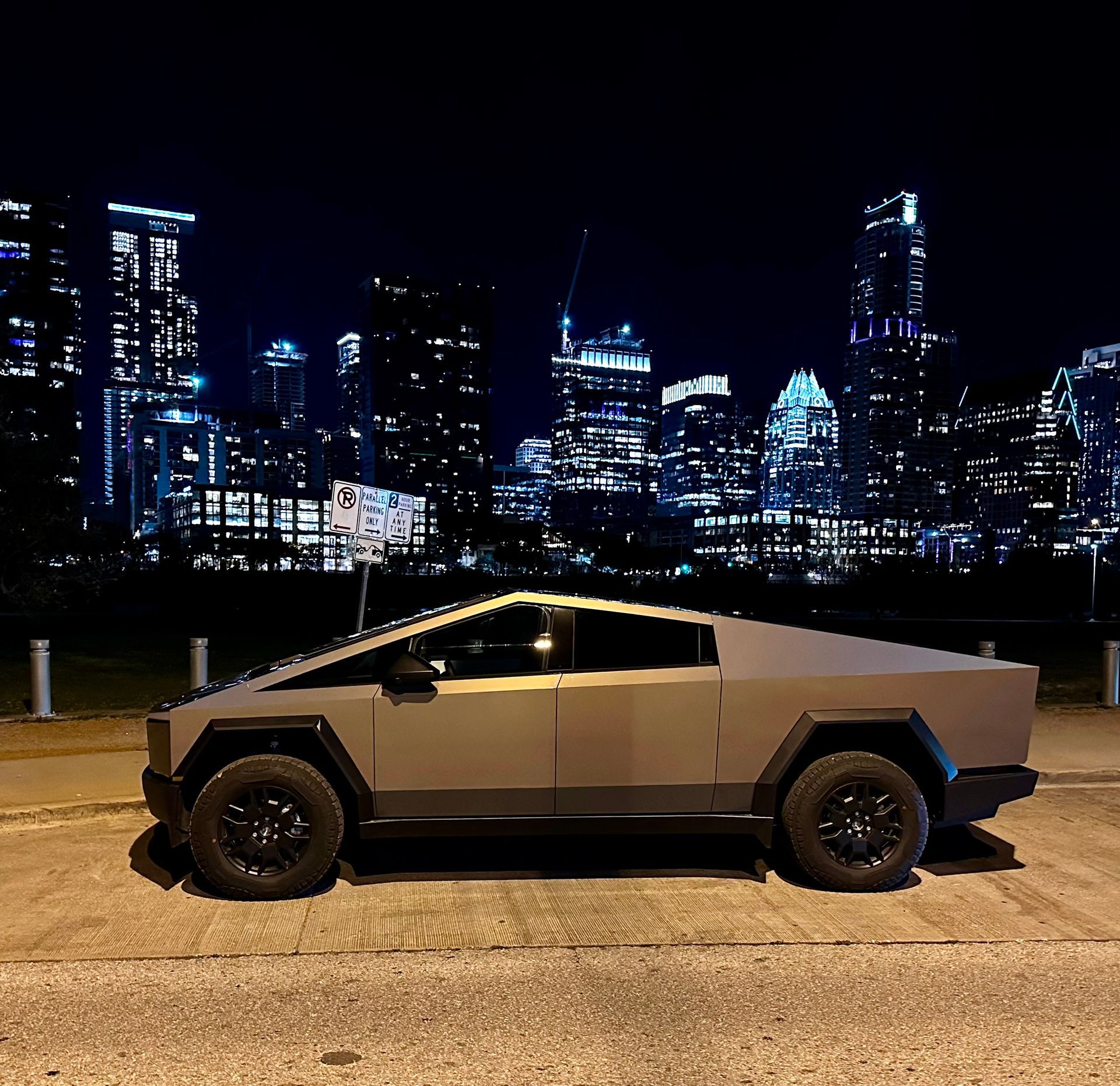 A tesla cybertruck is parked in front of a city skyline at night