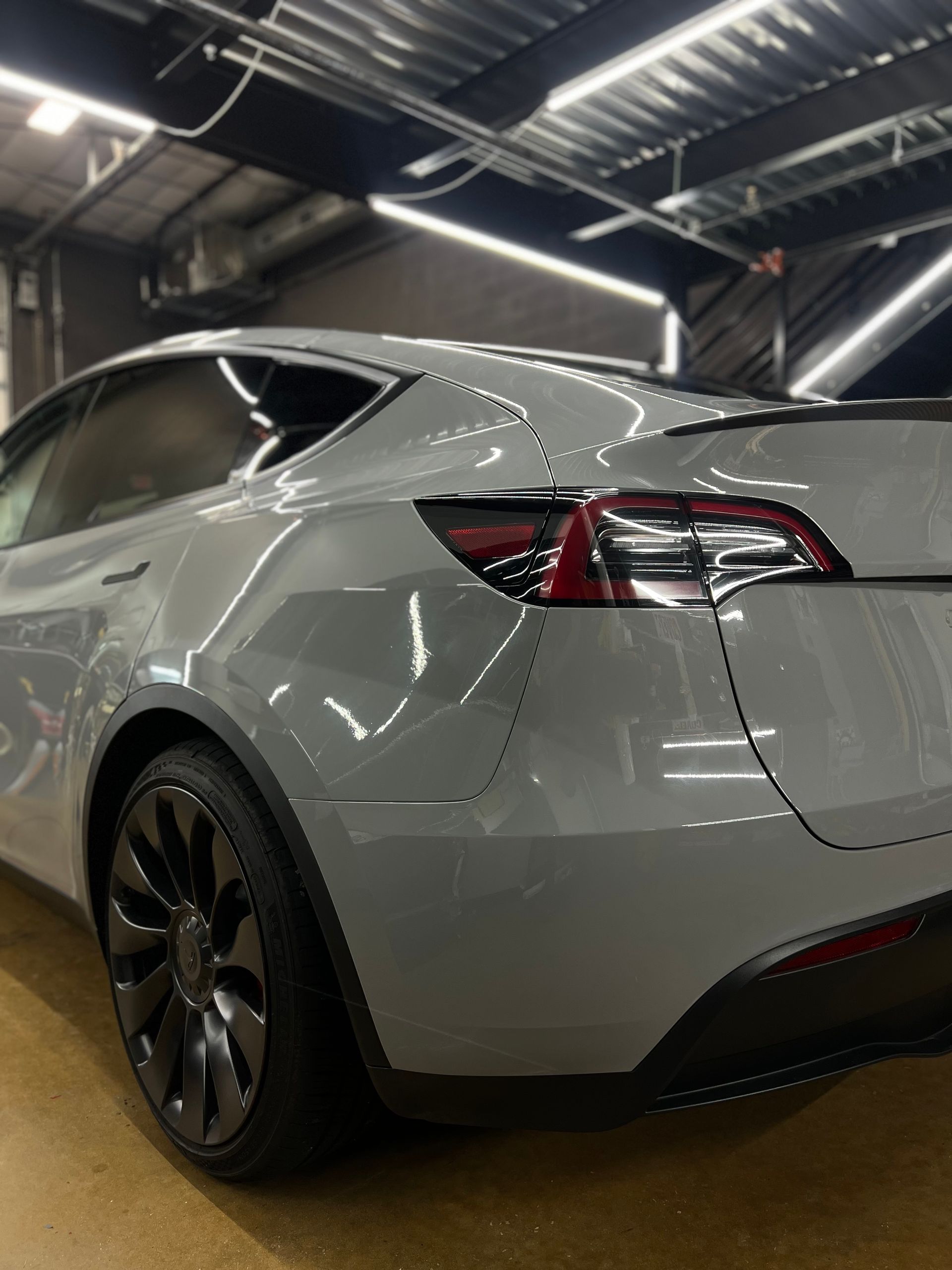 A gray tesla model 3 is parked in a garage.