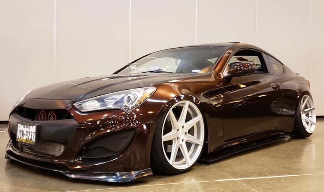A brown car with white wheels is parked on a concrete floor.