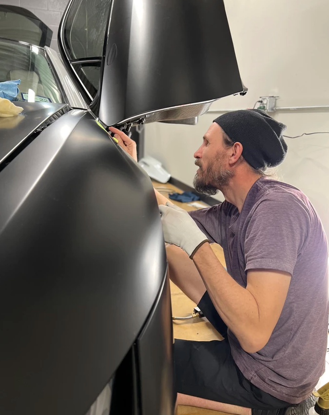 A man in a purple shirt is working on a black car