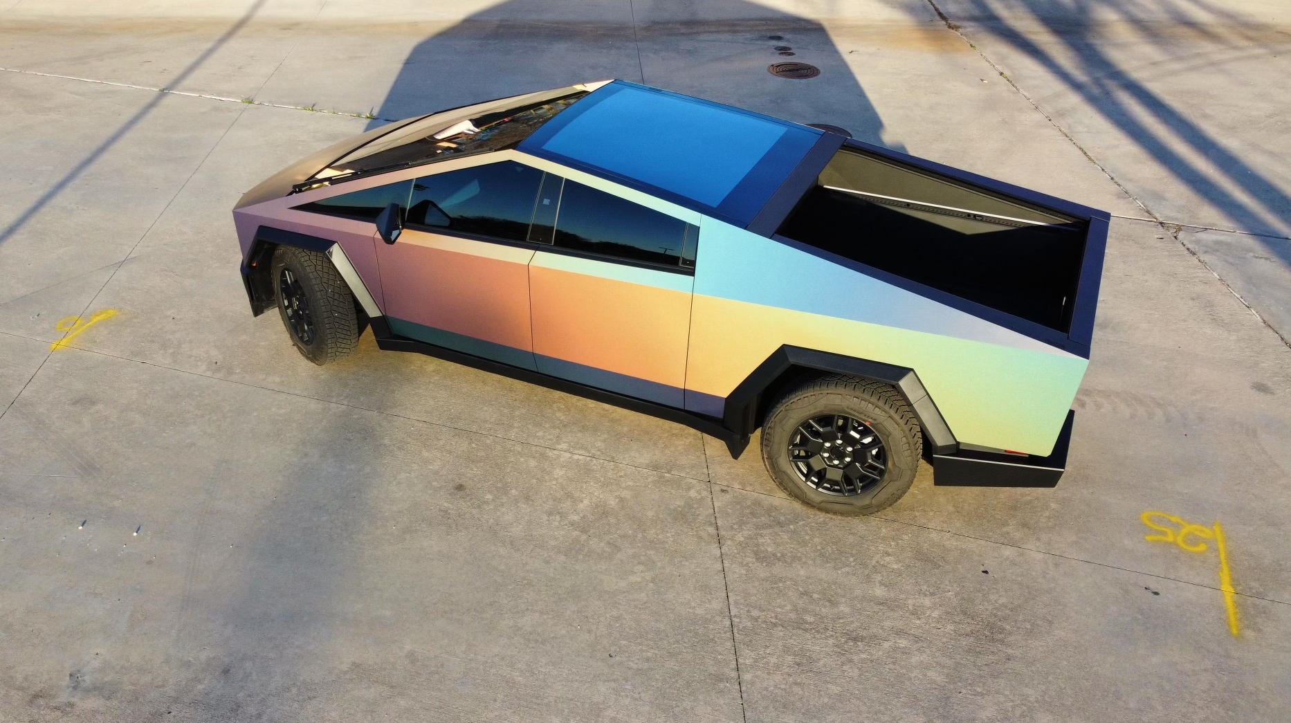 A rainbow colored tesla cybertruck is parked in a parking lot.