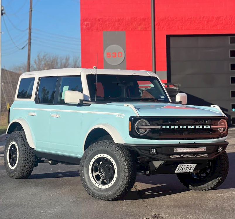 A light blue bronco is parked in front of a red building.